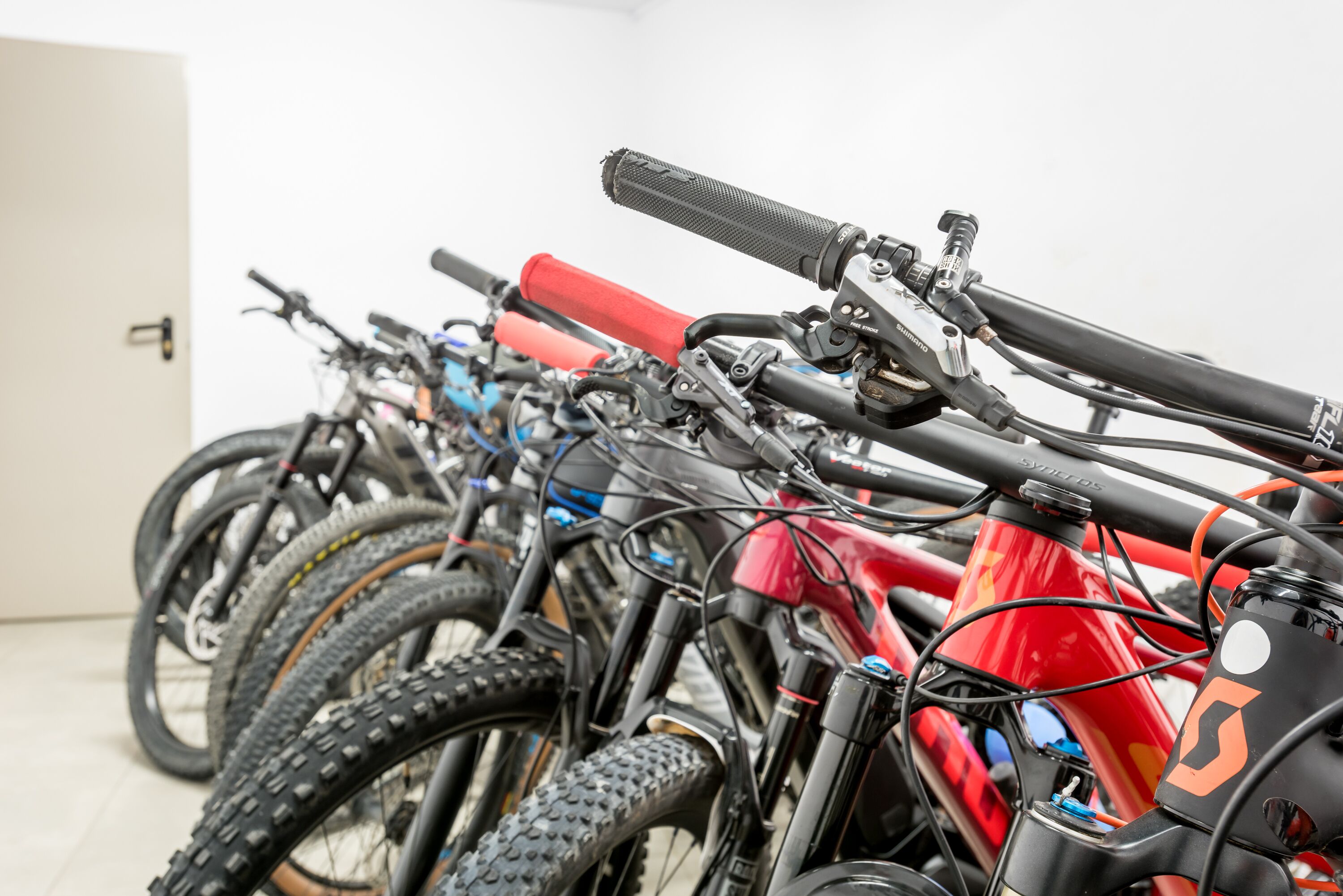 A row of bicycles parked indoors, with a white door in the background.