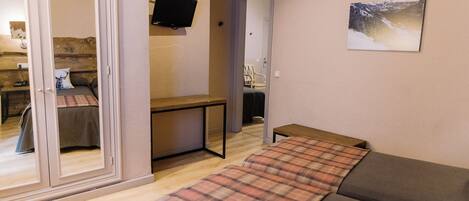 Una habitación con una cama, un escritorio, una silla y una televisión en la pared.