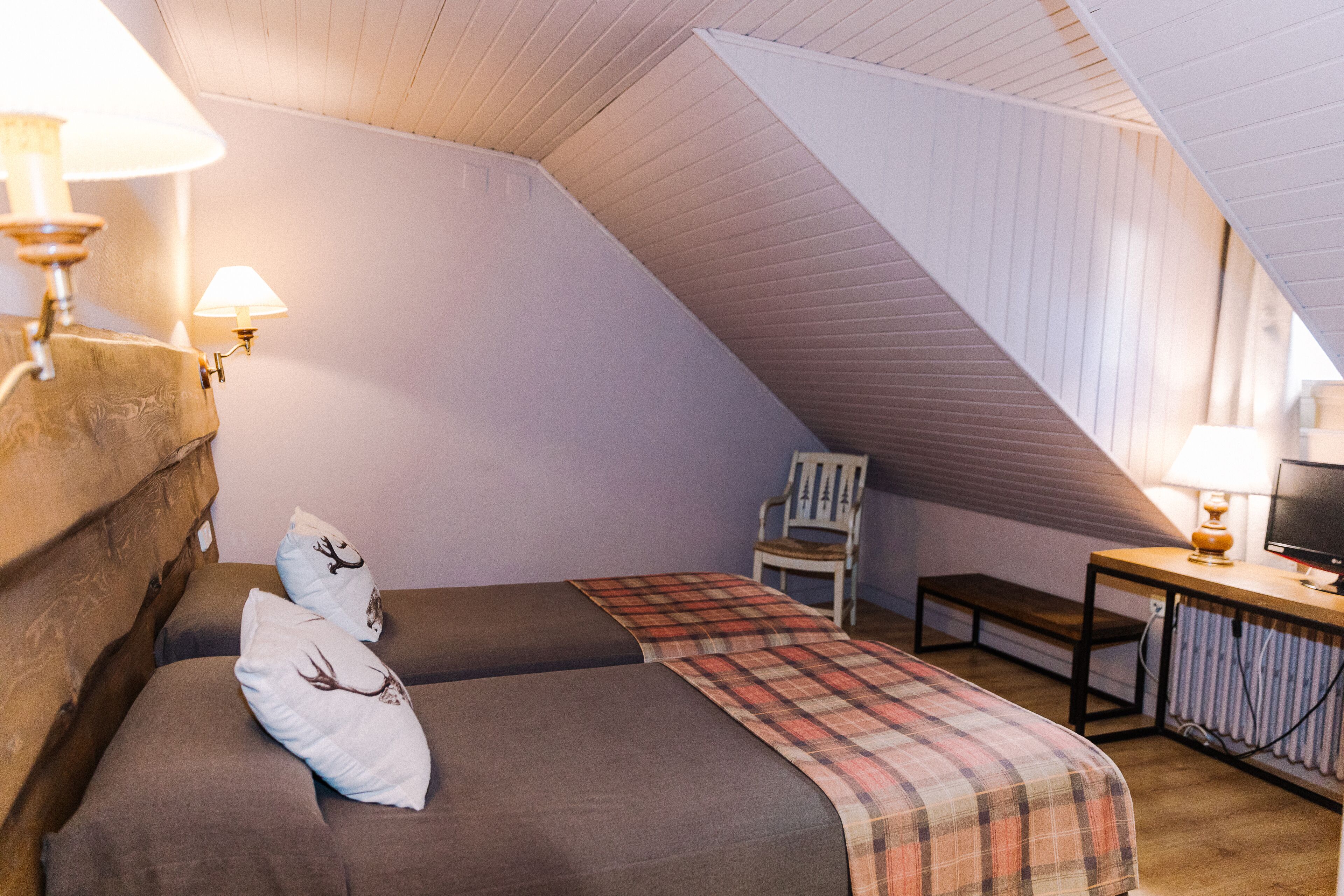 Une chambre mansardée chaleureuse, avec deux lits, une chaise, une table et une lampe.