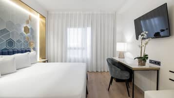 Habitación de hotel con cama, escritorio, silla, televisión y ventana con cortinas.