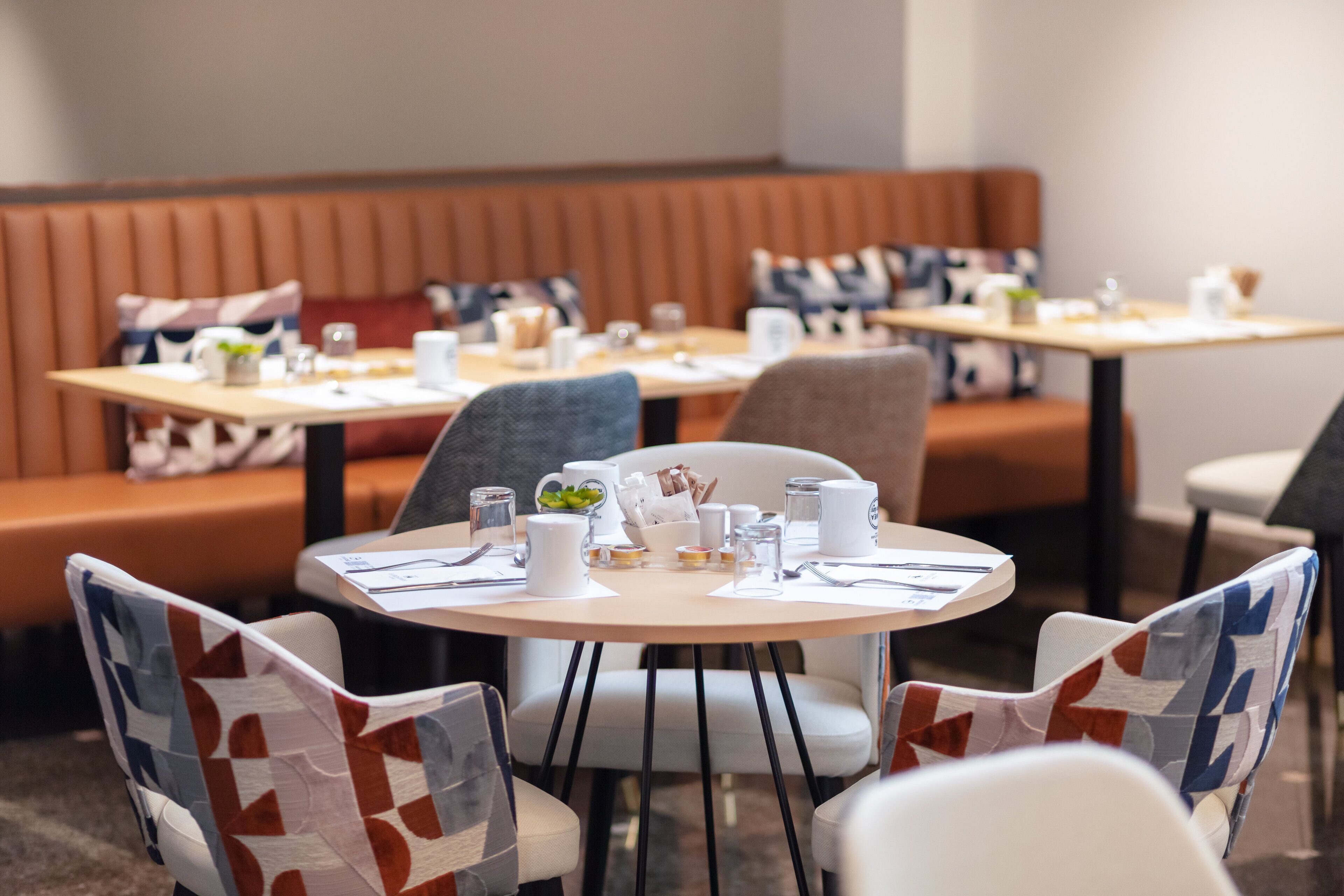 A restaurant with round tables, chairs with patterned upholstery, and a booth seating area.
