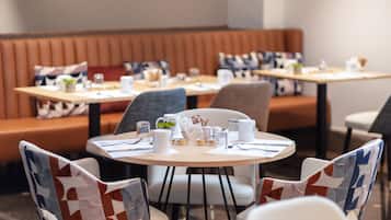 A restaurant with round tables, chairs with patterned upholstery, and a booth seating area.