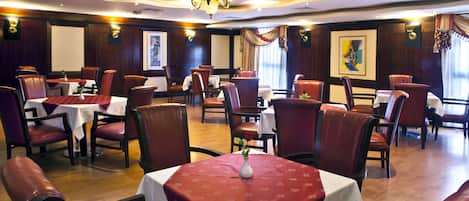 Un restaurante con mesas redondas cubiertas con manteles blancos, sillas rojas y un candelabro.