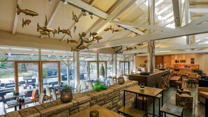 Un restaurant doté d’un coin salon avec un mur en pierre, de grandes fenêtres et de décorations en forme de poissons suspendues.