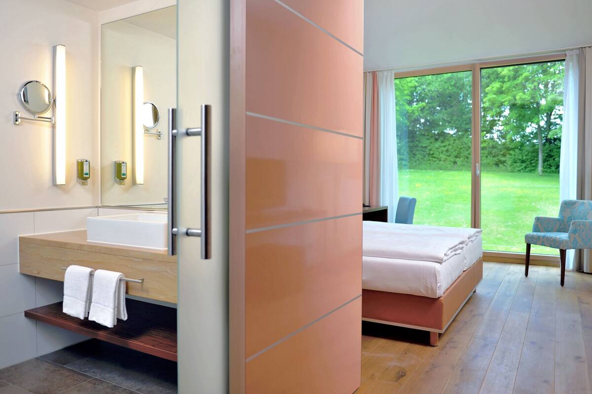 A modern bedroom with a large bed, a bathroom with a vanity, and a view of the outdoors.