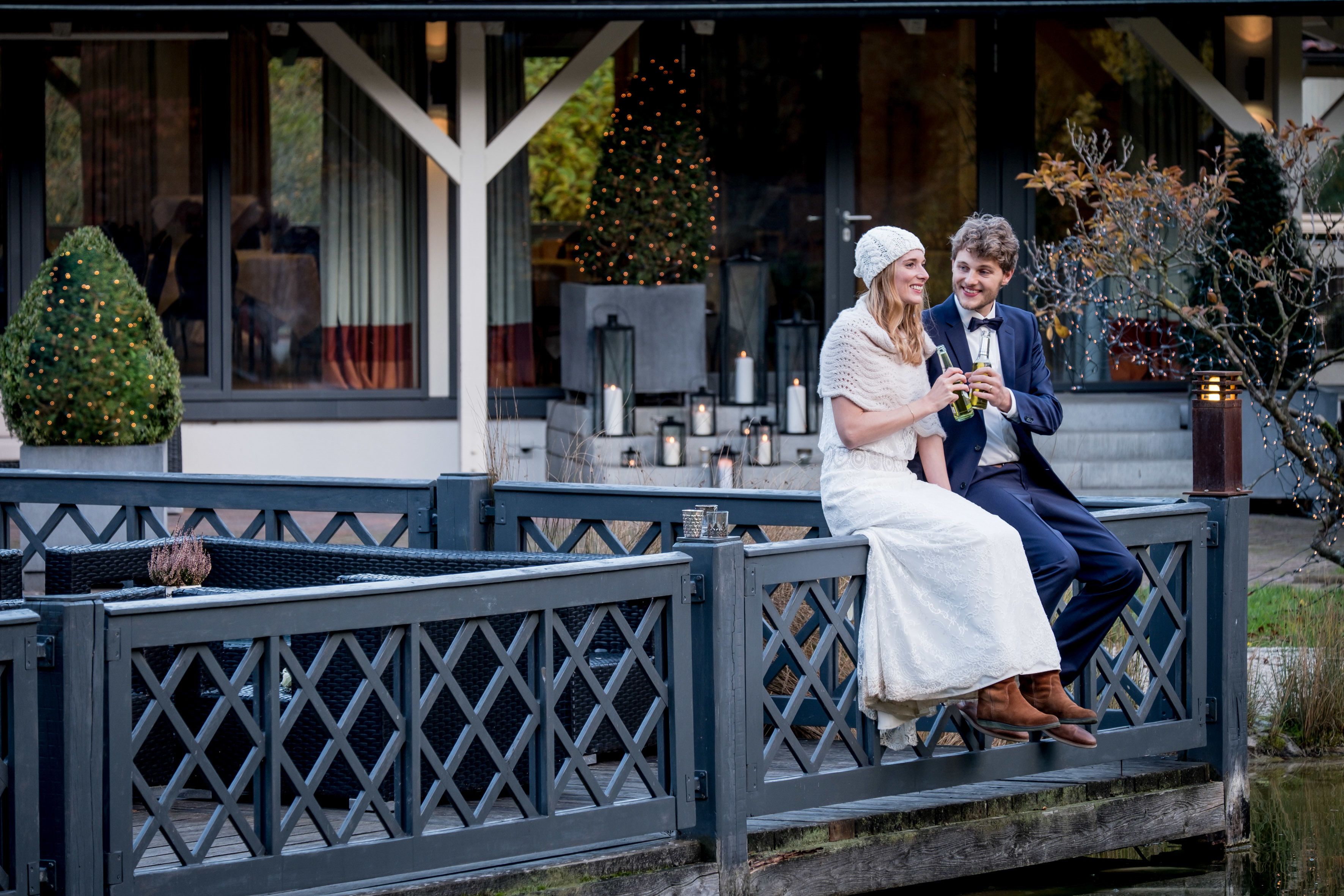 A couple sitting on a wooden bench outside a building with a Christmas tree and candles.
