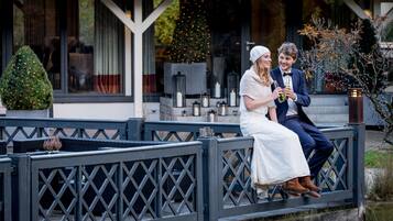 Una pareja sentada en un banco de madera frente a un edificio con un árbol de Navidad y velas.