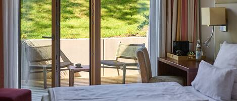 A hotel room with a bed, a desk, a chair, and a view of a grassy area through large sliding doors.