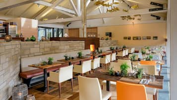 Ein geräumiges Restaurant mit hohen Decken, freiliegenden Balken und einer langen Theke mit mehreren Tischen und Stühlen.