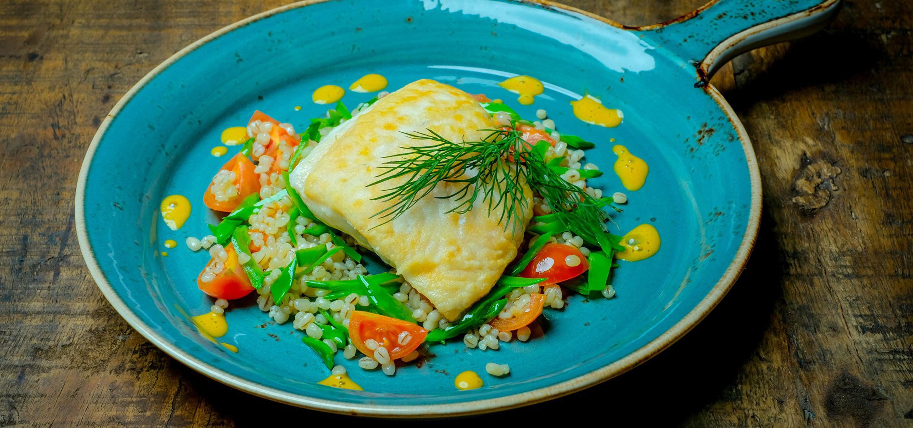 A blue plate with a piece of fish, vegetables, and grains.
