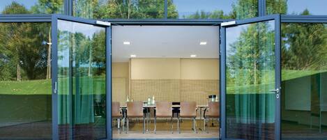 A modern room with glass walls, a tiled wall, and a seating area with tables and chairs.