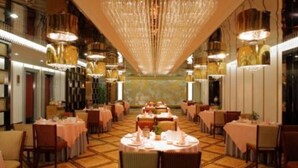 Uma ampla sala de jantar com mesas redondas, lustres e piso estampado.