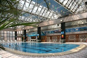An indoor swimming pool with clear lanes, surrounded by lounge chairs and a high ceiling with a glass structure.