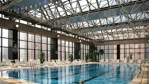 Piscina interior com pistas demarcadas, rodeada por espreguiçadeiras e grandes janelas.