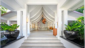 Un moderno vestíbulo de hotel con una escalera central, paredes blancas y grandes macetas negras con plantas tropicales.