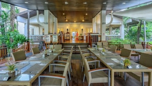 A spacious outdoor dining area with multiple tables and chairs, surrounded by lush greenery.