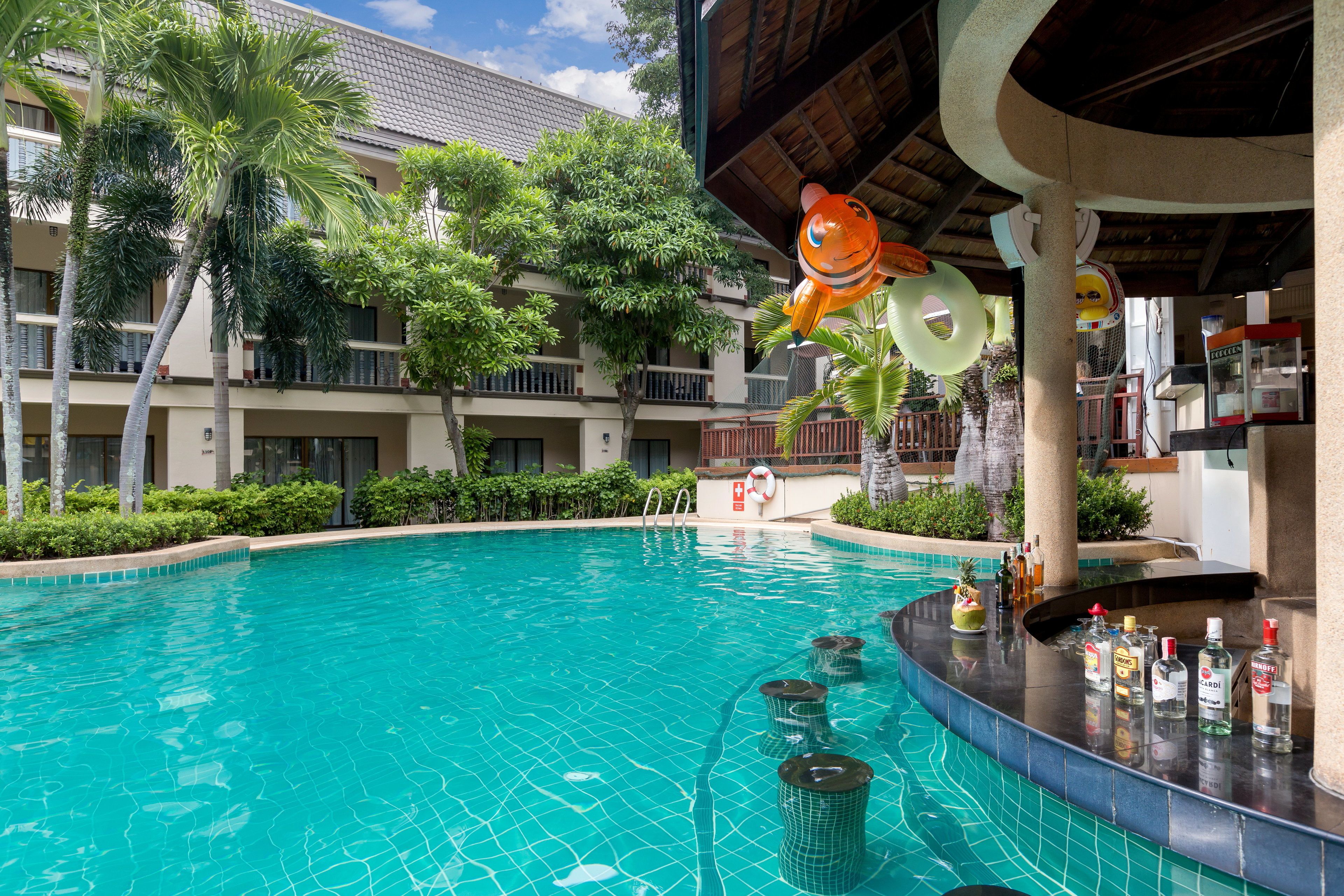 A swimming pool with a bar area, palm trees, and a building with balconies.