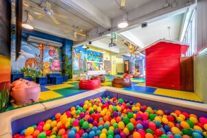 Un área de juegos interior llena de color con piscina de pelotas, estructuras de juego y un mural de animales.