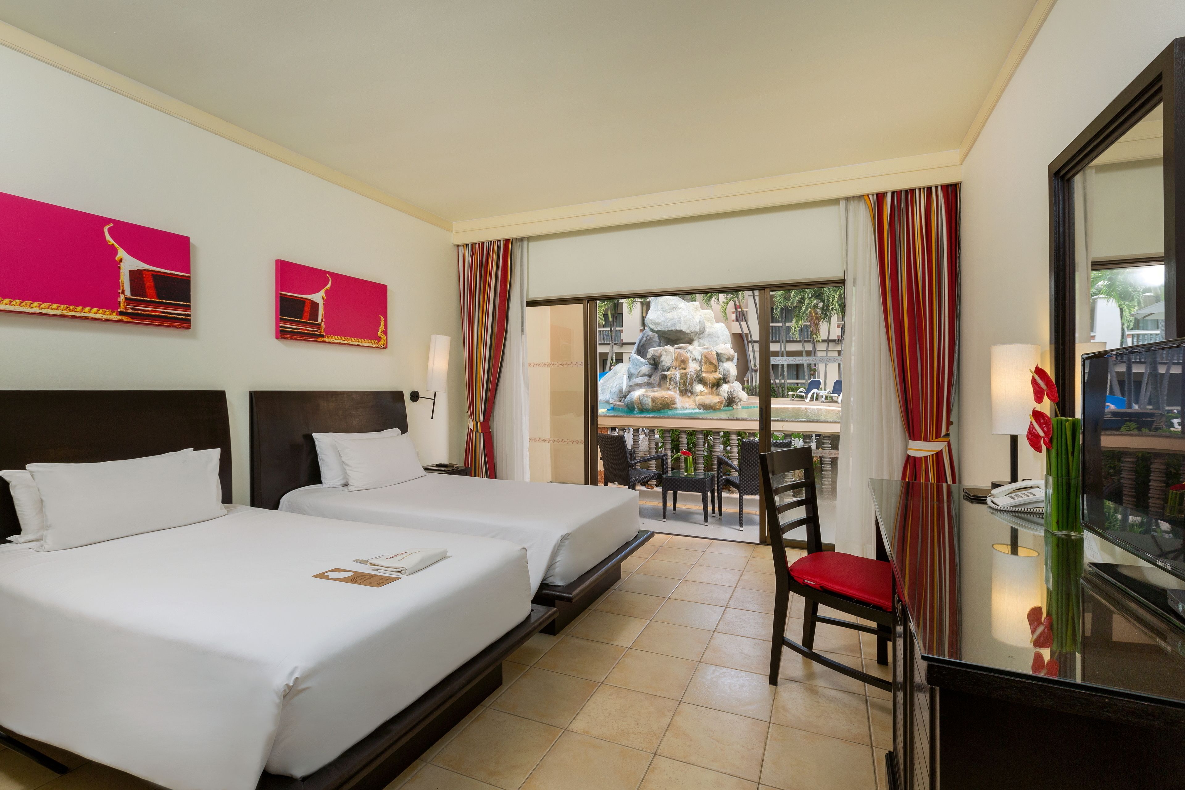A hotel room with two beds, a balcony with a view, and a dining area with chairs and a table.