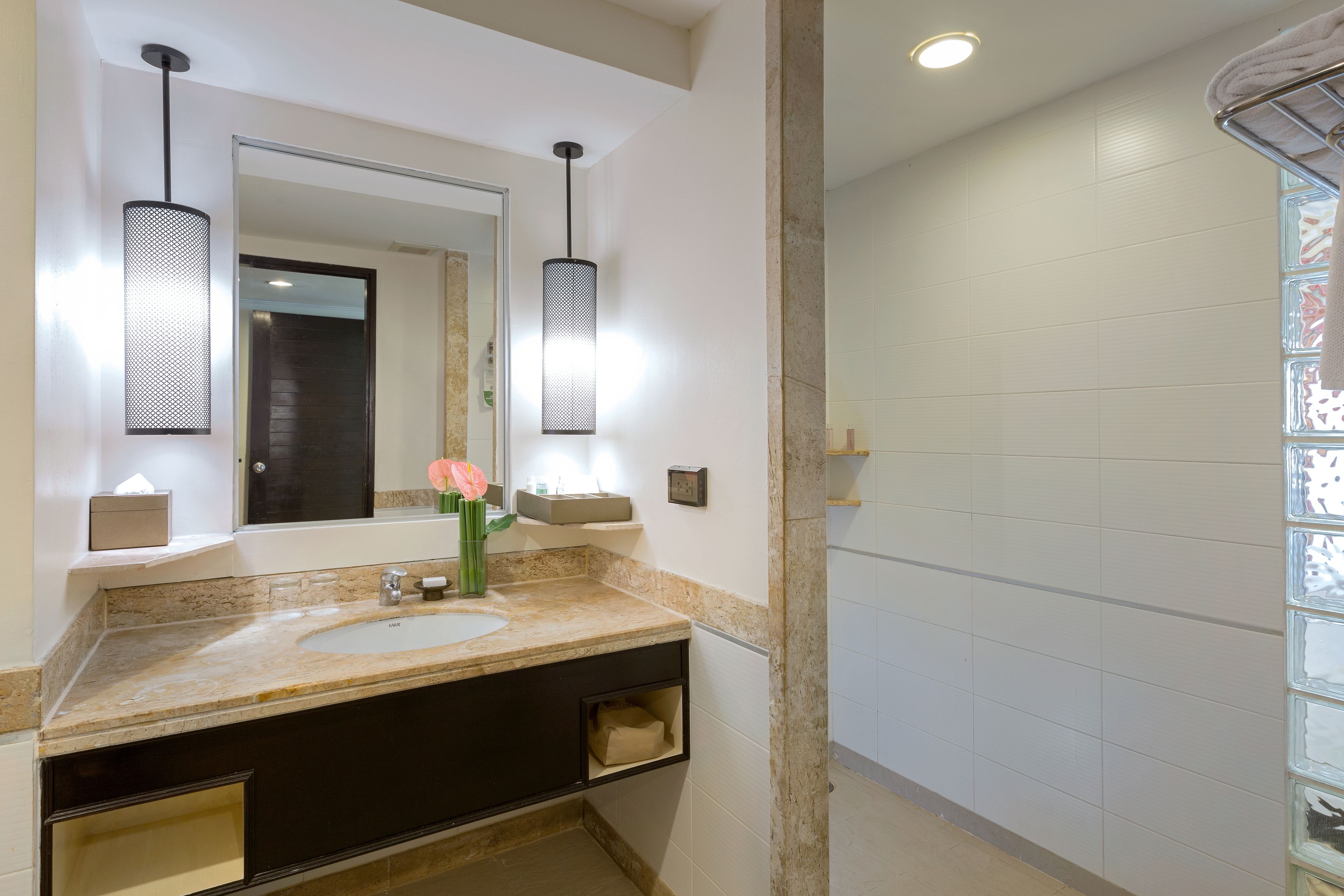 A bathroom with two sinks, a large mirror, pendant lights, and a shower area.