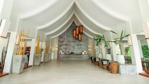 A spacious lobby with a reception desk, seating area, and decorative elements like bamboo sticks and plants.