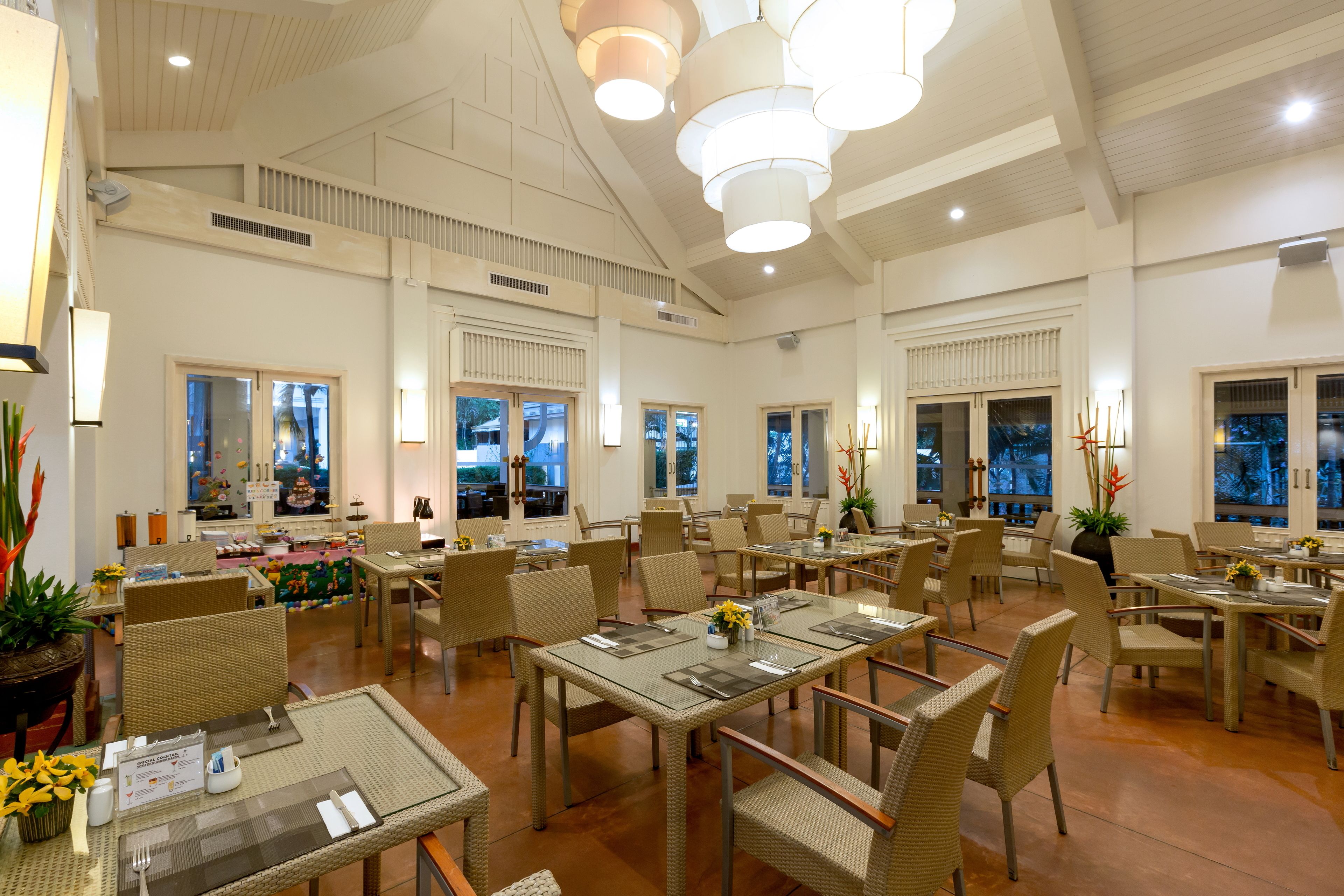 A spacious dining area with multiple tables and chairs, large windows, and ceiling lights.