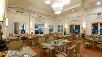 A spacious dining area with multiple tables and chairs, large windows, and ceiling lights.