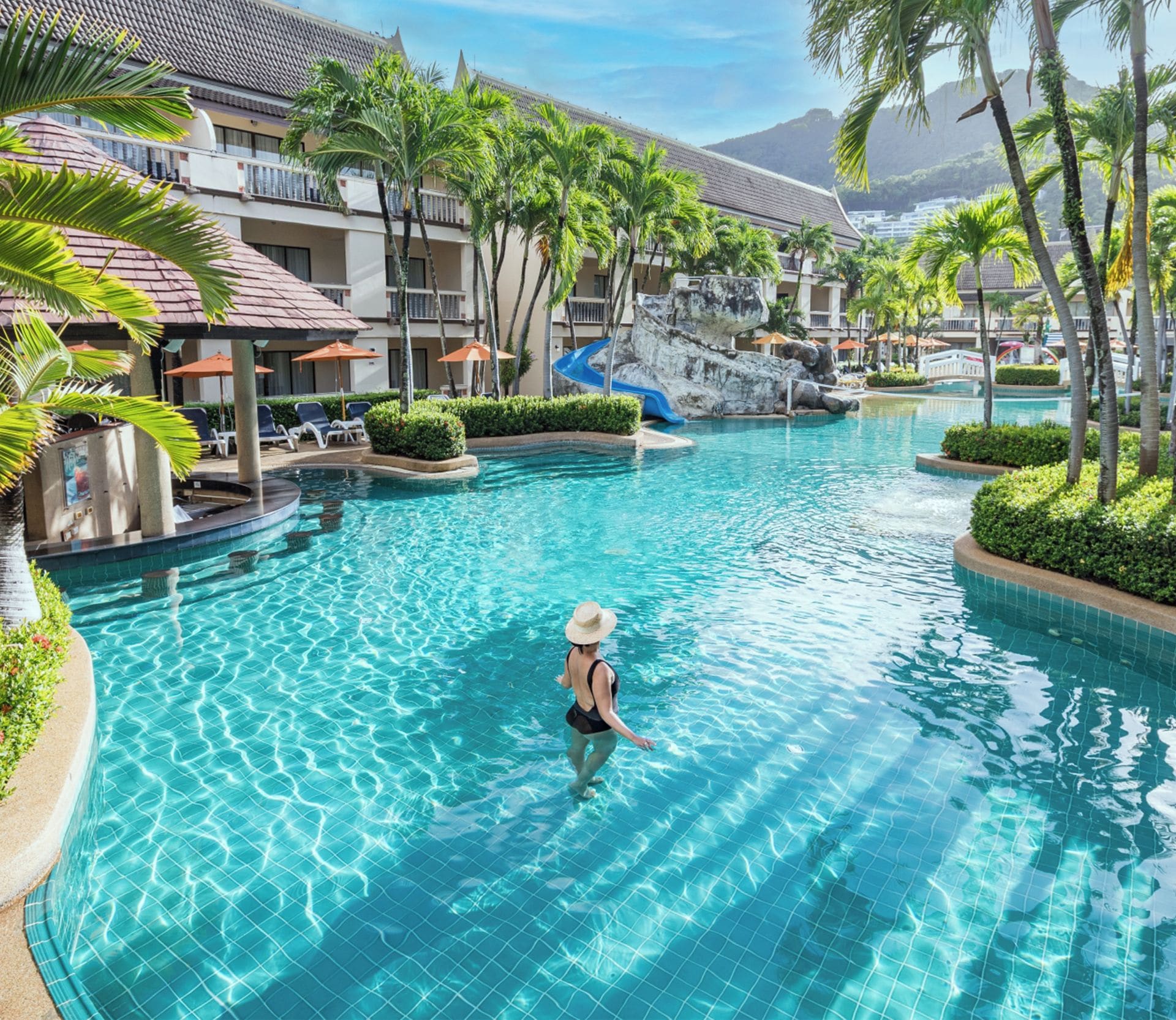 A swimming pool at Centara Kata Resort Phuket with clear water, palm trees, and a person swimming.