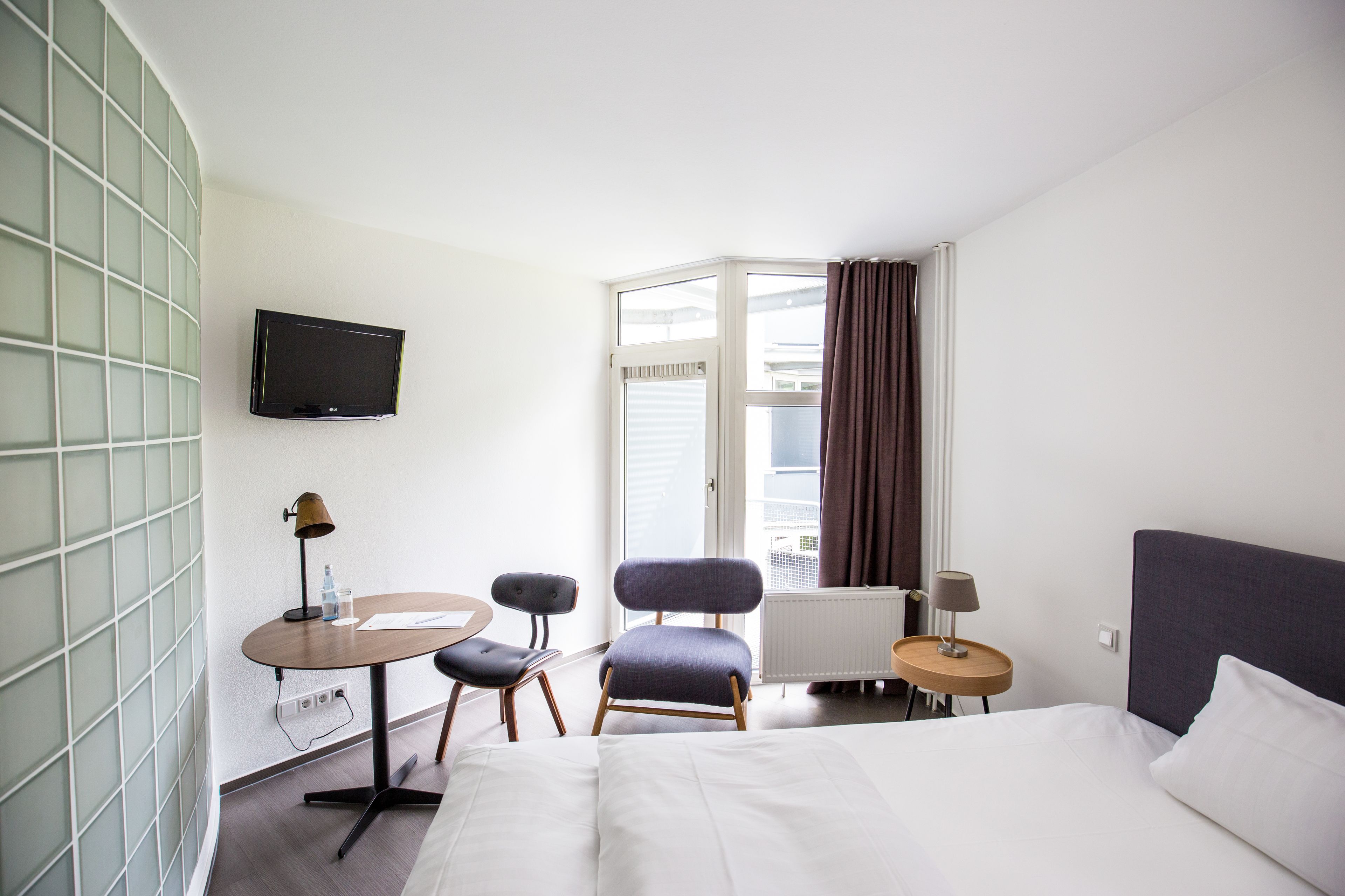 A hotel room with a bed, a desk with a chair, a television, and a window with curtains.