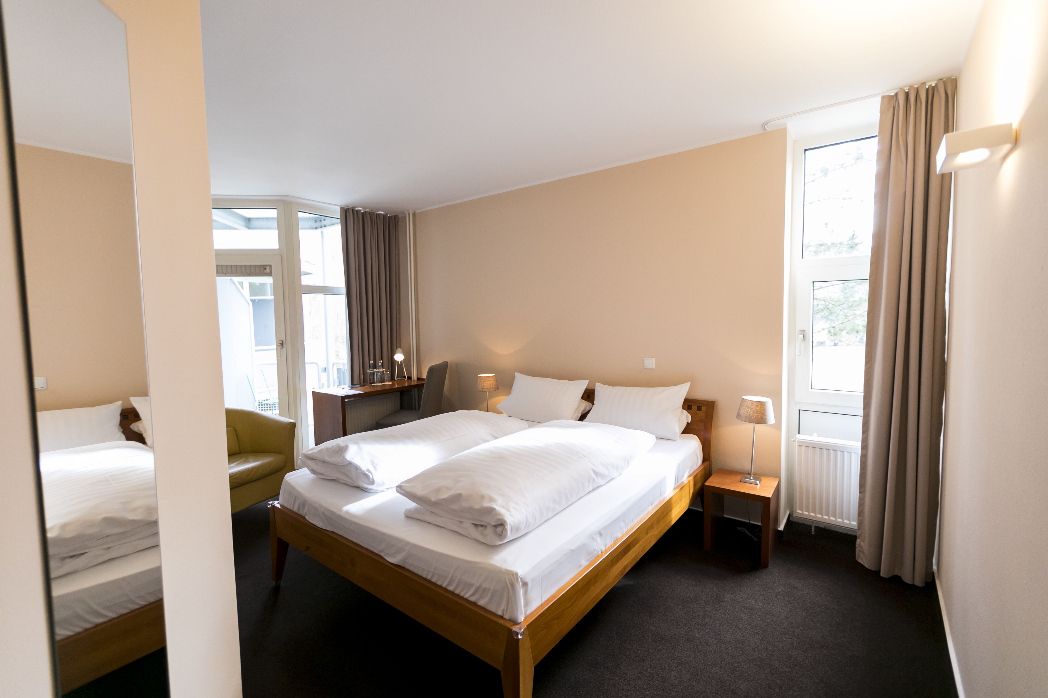 Ett hotellrum med två sängar, en stol, ett skrivbord och ett fönster med gardiner.