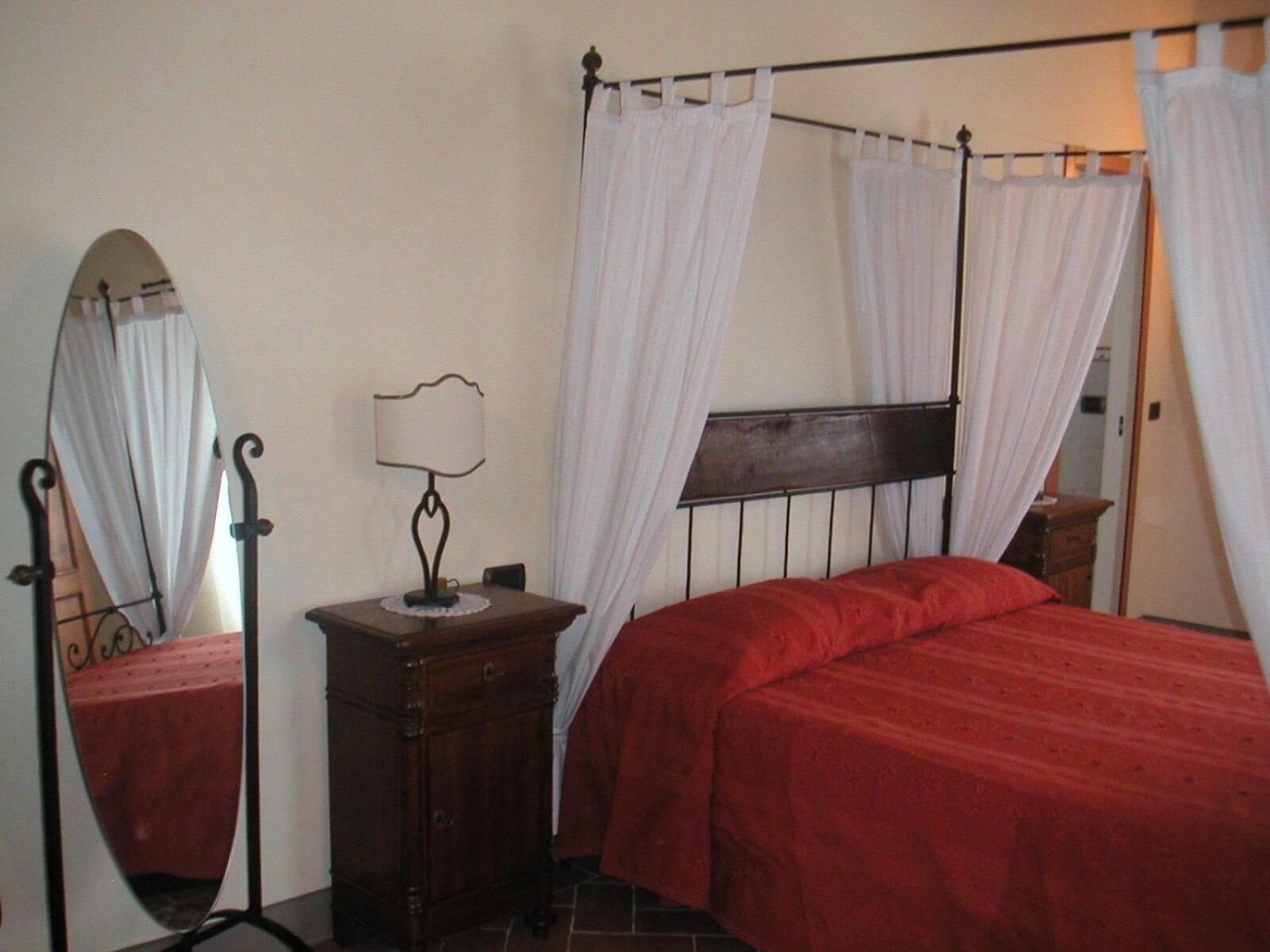 A bedroom with a wooden bed, a nightstand, a lamp, and a mirror.