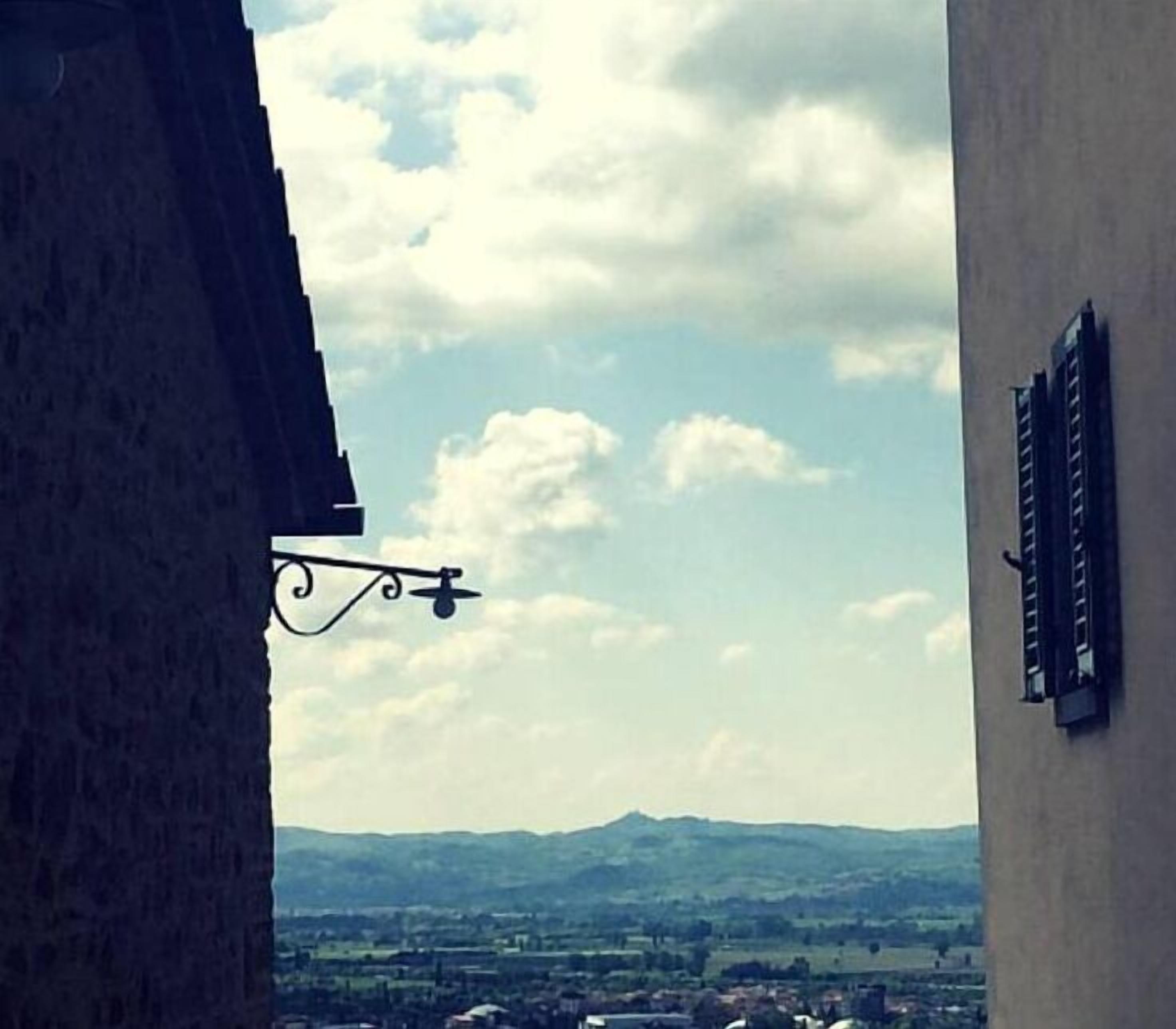 Vista desde una ventana de edificio hacia un paisaje con montañas distantes y un cielo parcialmente nublado.
