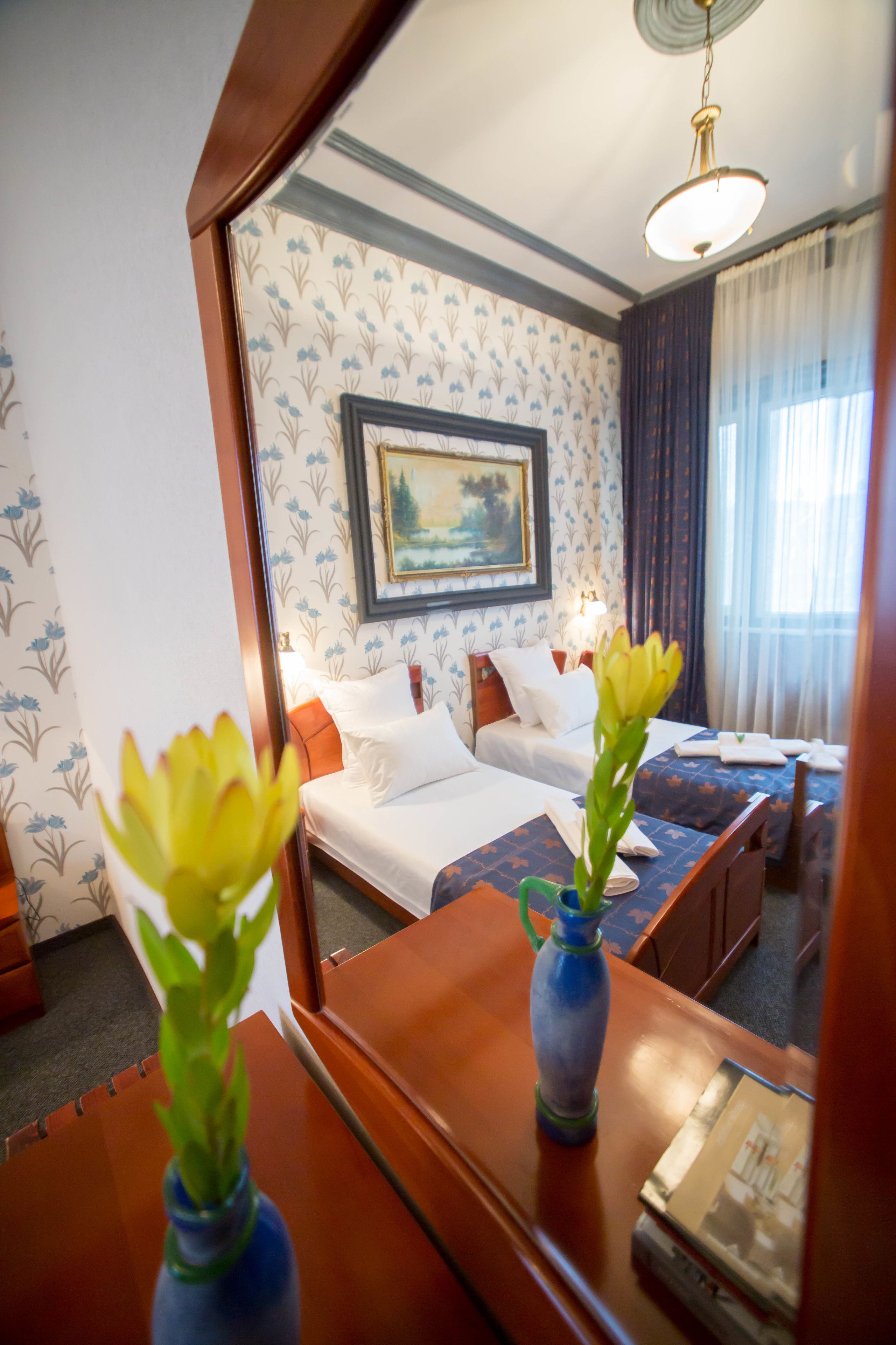 A hotel room with two beds, a painting on the wall, and a vase with flowers on the table.