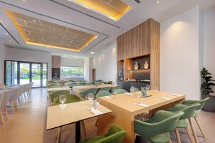 Un comedor moderno con varias mesas y sillas, ventanas amplias y una pared de acento de madera.