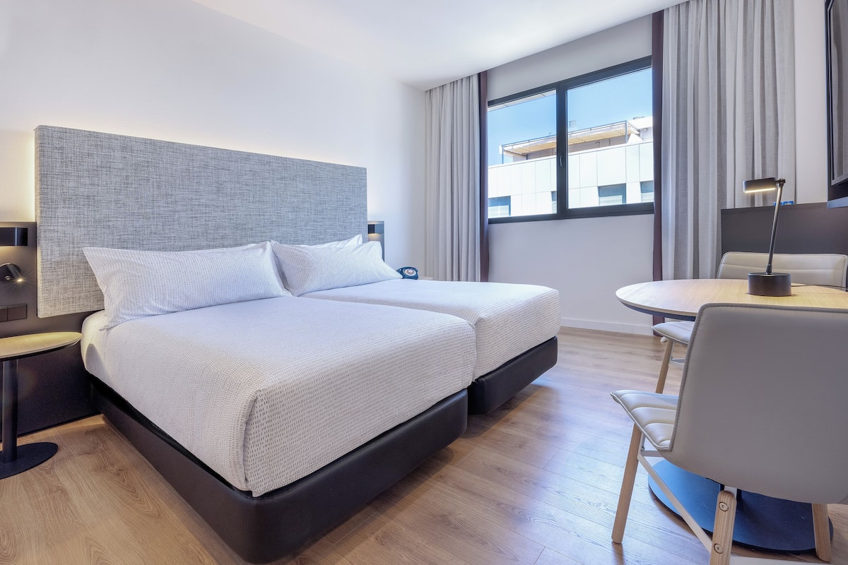 Una habitación de hotel moderna con una cama grande, mesitas de noche, un escritorio y una silla.