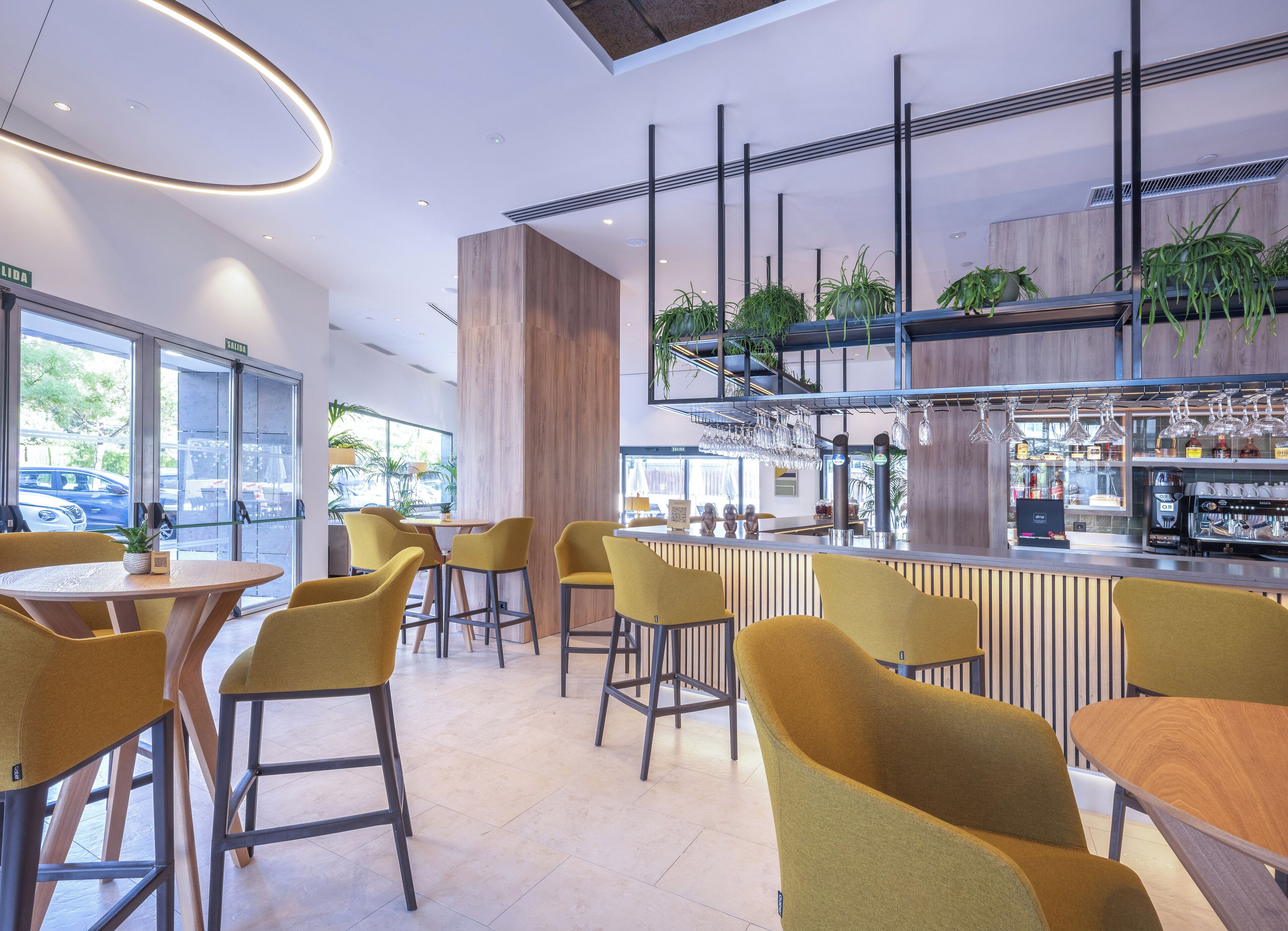 Zona de bar moderna con sillas amarillas, una barra con máquina de café y plantas.