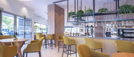 Zona de bar moderna con sillas amarillas, una barra con máquina de café y plantas.