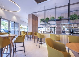 Zona de bar moderna con sillas amarillas, una barra con máquina de café y plantas.
