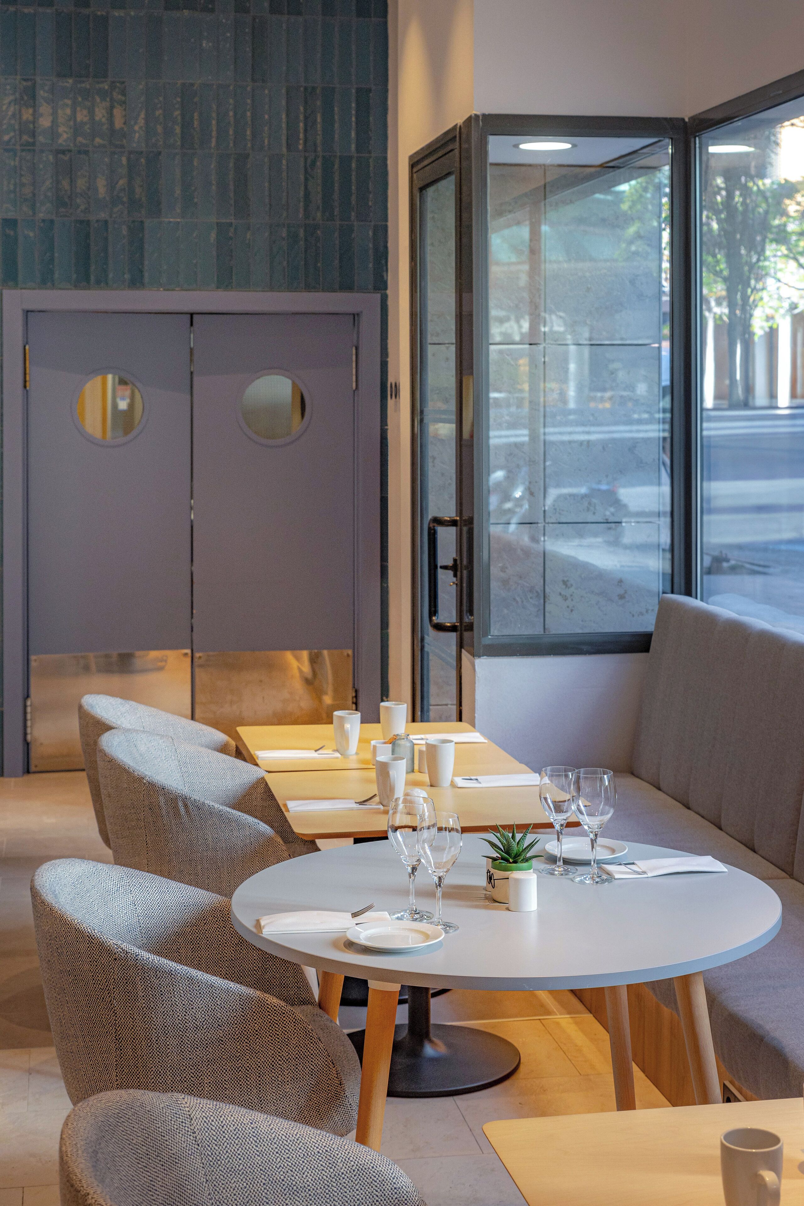 A modern dining area with round tables, cushioned chairs, and a view through a glass door.