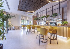 Een moderne bar met gele stoelen, een houten toonbank en potplanten.