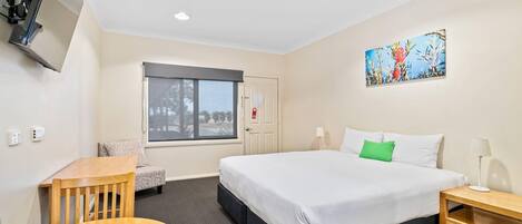 Une chambre d’hôtel avec un lit, un bureau, une chaise, une fenêtre et un tableau au mur.