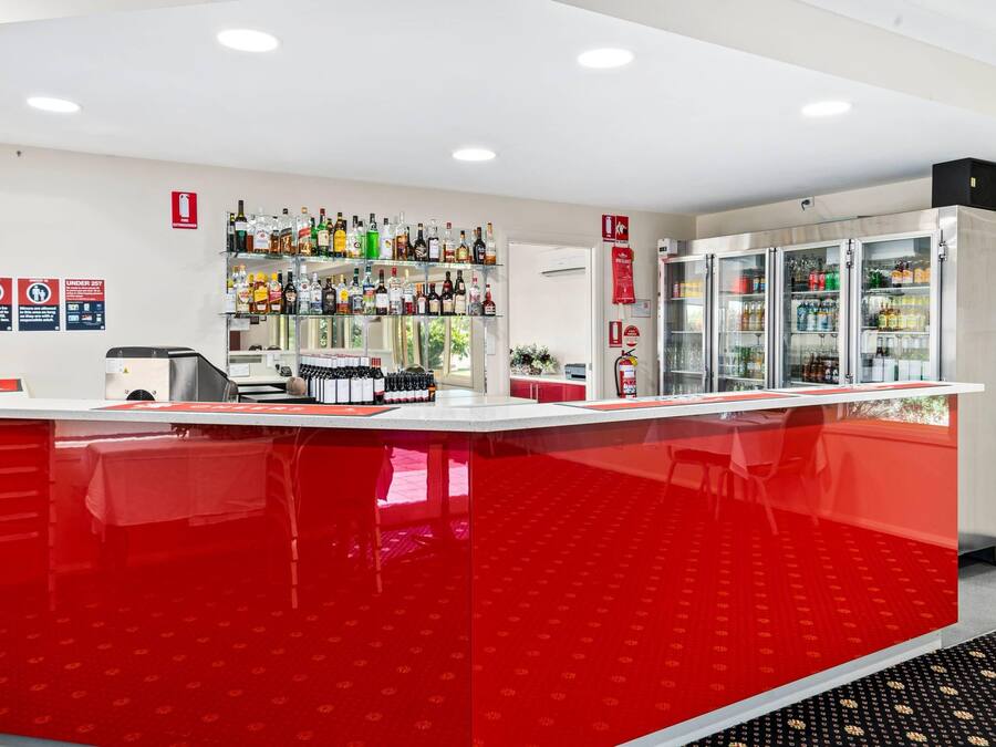 Zona de bar con mostrador rojo, estantes llenos de botellas de licor y un refrigerador.