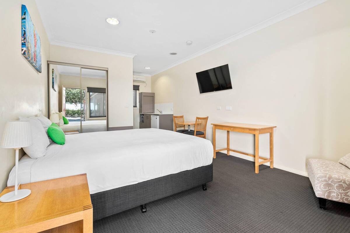 A hotel room with a large bed, a desk, a chair, a TV, and a view of the outside.