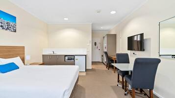 Ett hotellrum med en säng, ett skrivbord, en mikrovågsugn, en TV och ett litet pentry.
