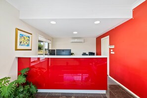 A reception desk with a red counter, a framed artwork above it, and an air conditioning unit on the wall.
