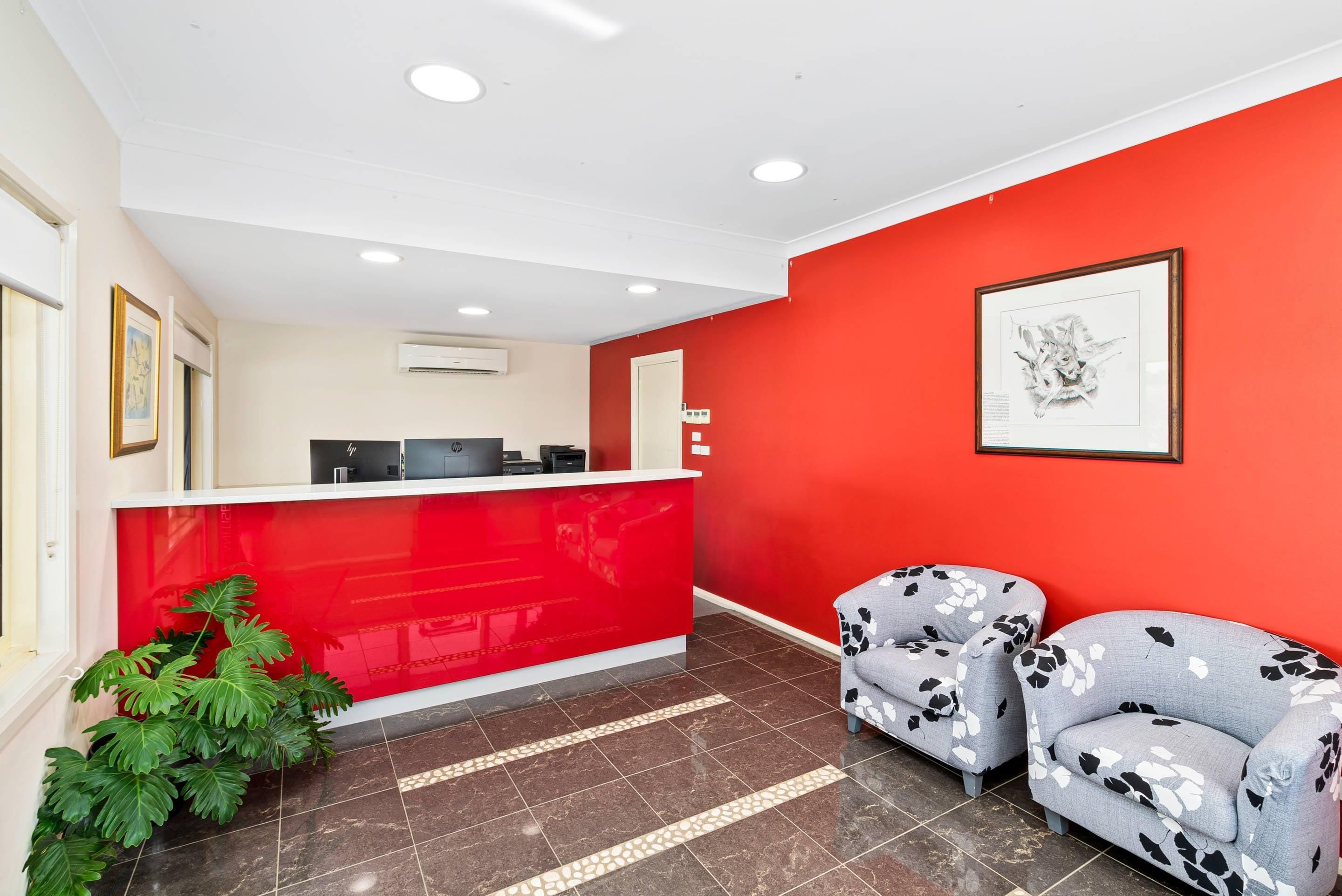 A reception area with a red wall, a reception desk, two patterned sofas, and a potted plant.