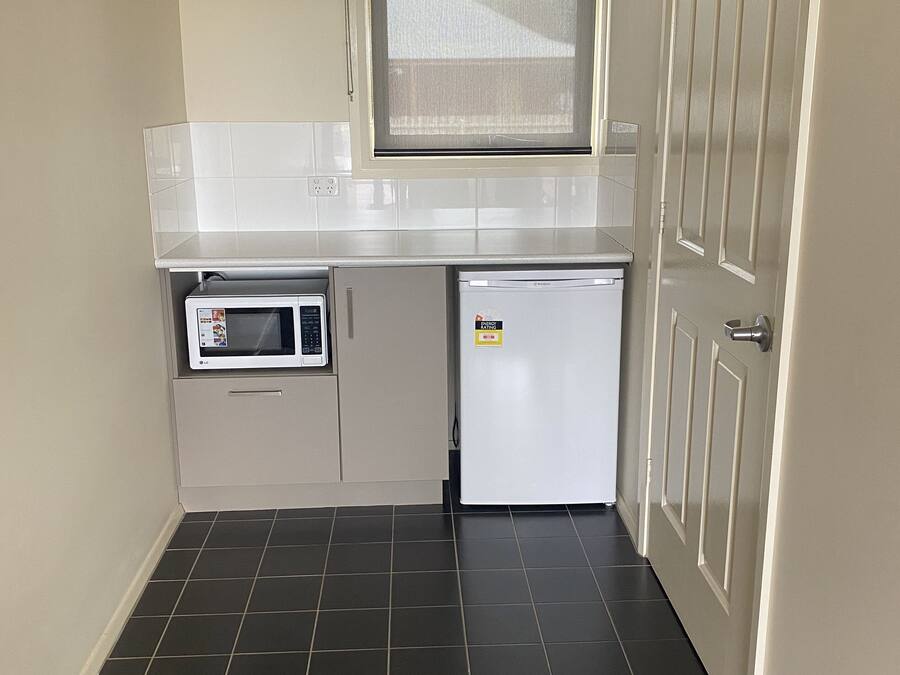 Una cocina compacta equipada con microondas, refrigerador y ventana sobre el lavamanos.