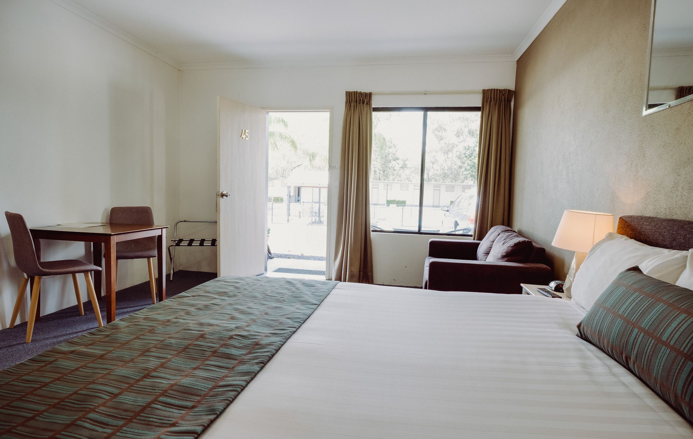 Een hotelkamer met een bed, een bureau, een stoel, een bank en een raam met gordijnen.