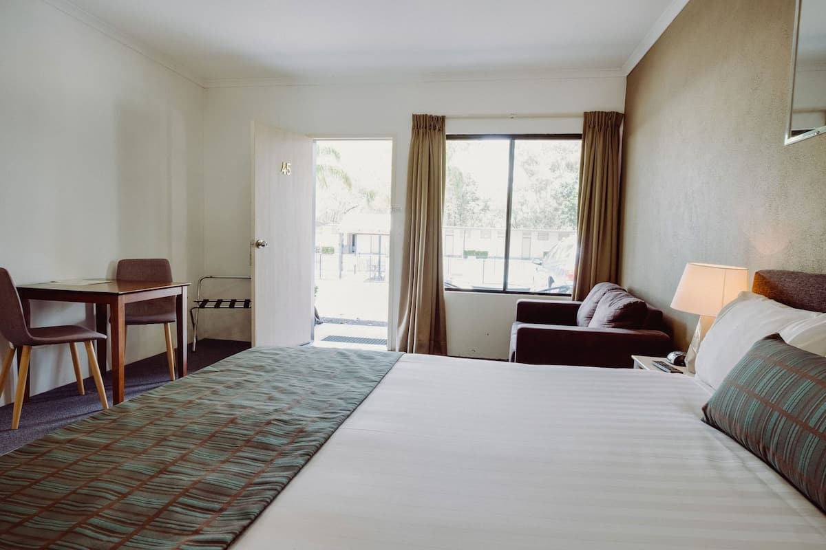 A hotel room with a bed, a desk, a chair, a sofa, and a window with curtains.