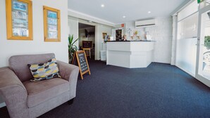 A reception area with a reception desk, a couch with patterned cushions, and framed pictures on the wall. - Artesian Spa Motel (Moree)